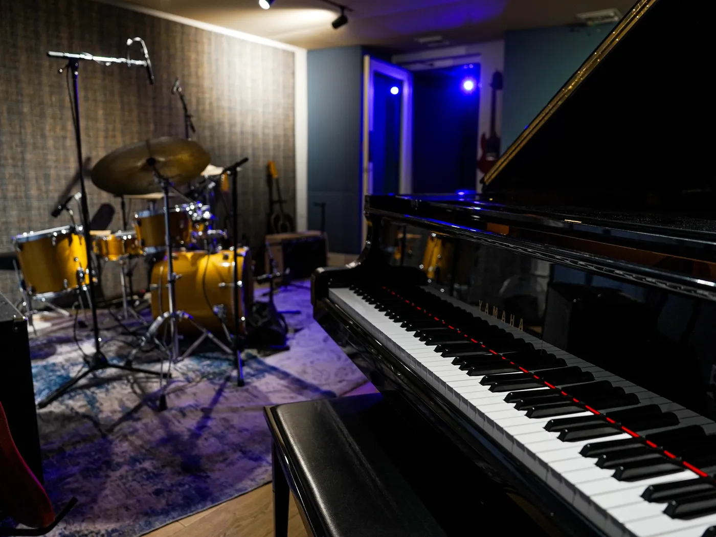 A rehearsal room at the Club: grand piano keys in the foreground, a drum kit on the rug behind
