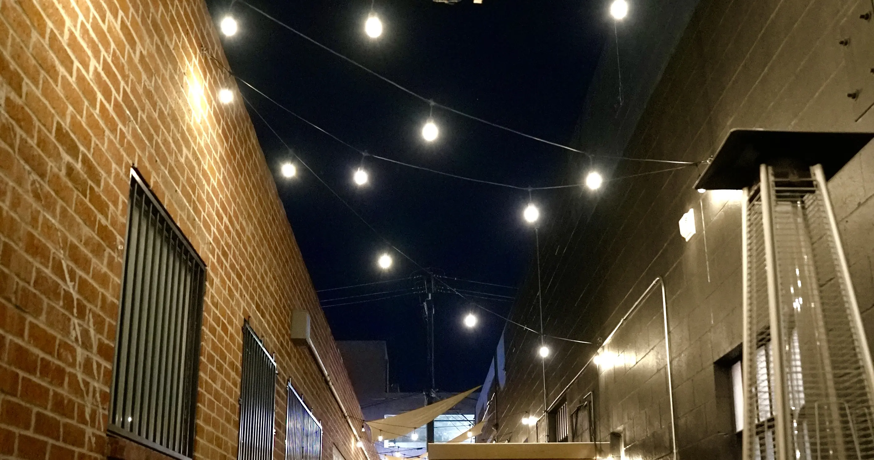 The patio at night, string lights strung against the sky between a brick wall and the heaters