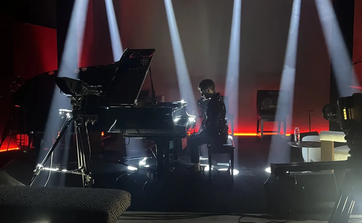 A pianist at the grand piano on the Live Room stage, under five moving-head beams