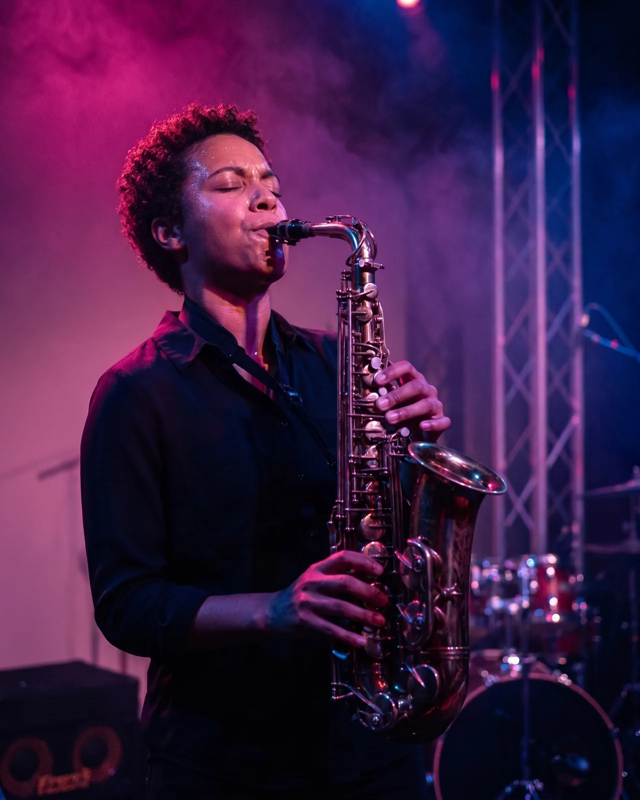 A saxophonist mid-solo, eyes closed, lit magenta and blue in the haze