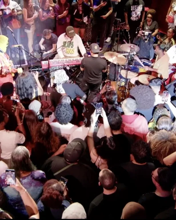 A packed room at a live night, the crowd pressed in around the band, phones up