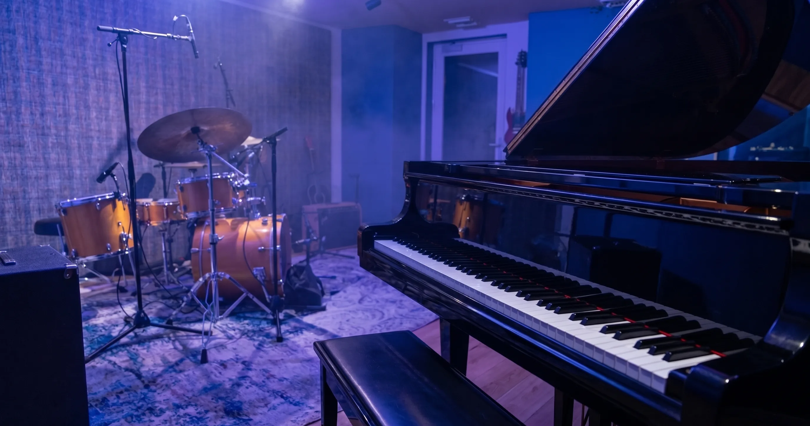 The Recording Room under a deep blue wash: the grand piano's keys in the foreground, the drum kit mic'd on its rug in the haze behind
